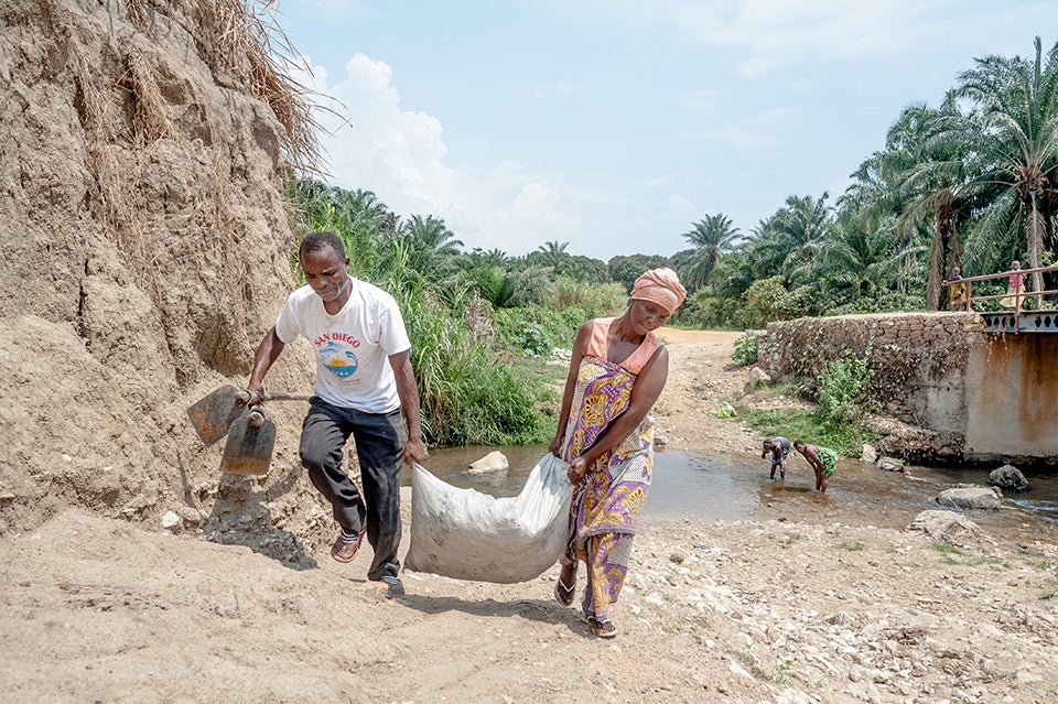 With the help of a camp worker, Luscie, right, hauls rock and clay from a river back to a UN Women multipurpose centre for use in building a clay stove. UN Women has established three Safe Haven multipurpose centres, which offer psychosocial counselling, referrals, skills training and cash-for-work programmes.  Photo: UN Women/Catianne Tijerina